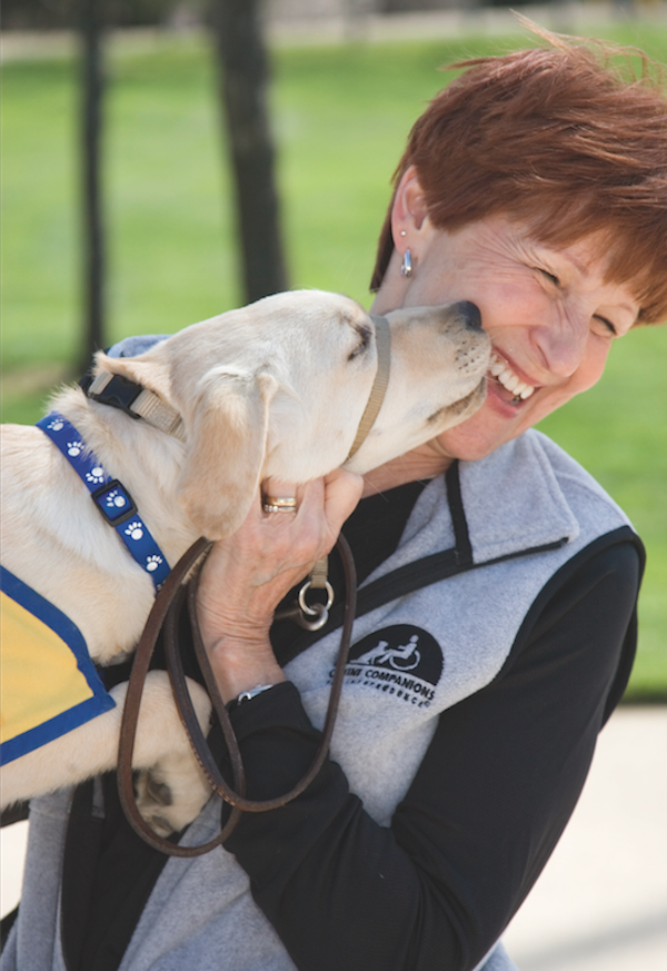 A puppy raiser with CCI gets canine kisses. (Photo courtesy Canine Companions for Independence)