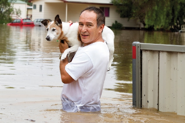 Man wading in flood, carrying dog. 