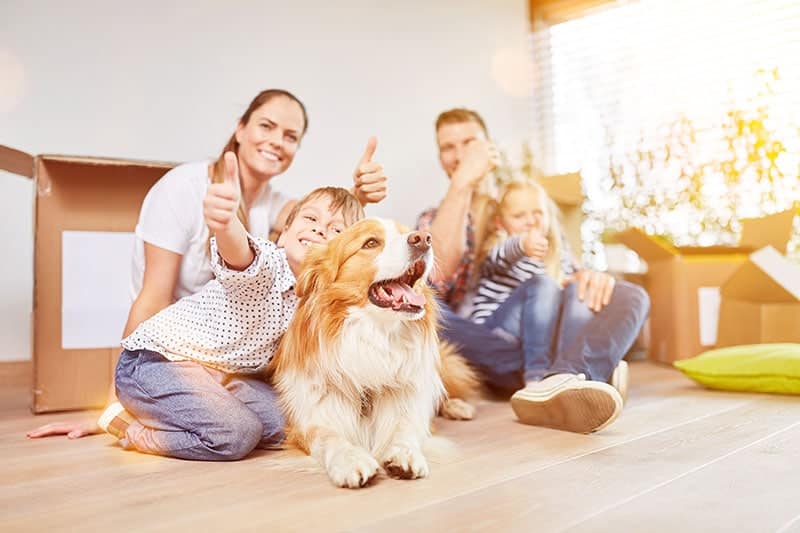 Happy-family-with-two-kids-and-dog-holds-thumbs-up-in-new-home