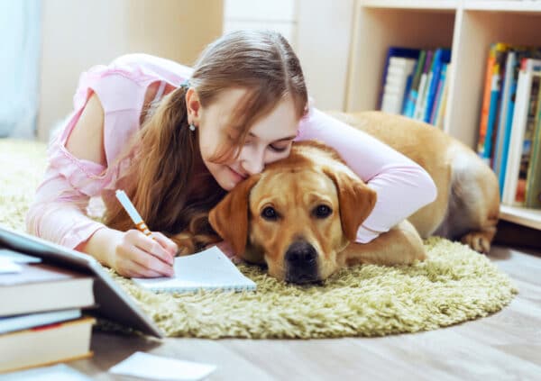 Teenage girl embracing pet dog while doing homework