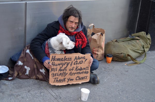 A homeless man with a dog and a sign.