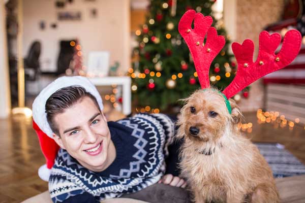 A man and his dog dressed in holiday / Christmas gear.