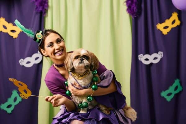 Young woman in Mardi Gras costume having fun with her dog on a party and looking at camera