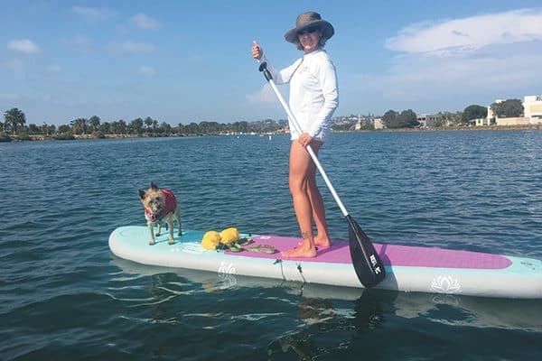 A woman stand up paddleboarding with her dog.