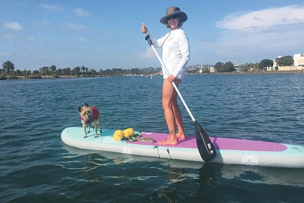 A woman stand up paddleboarding with her dog.