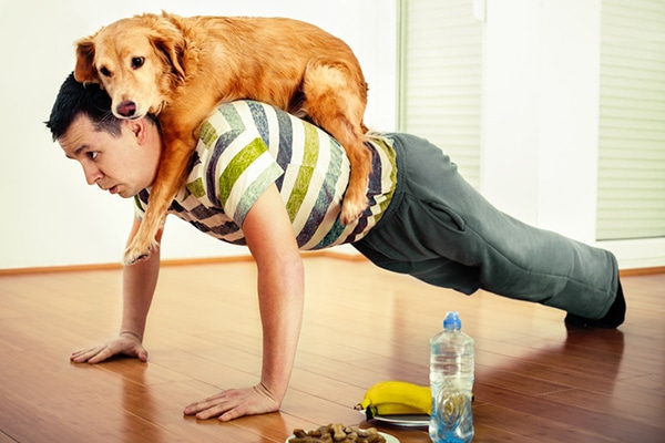 A man doing pushups exercises with his dog. 