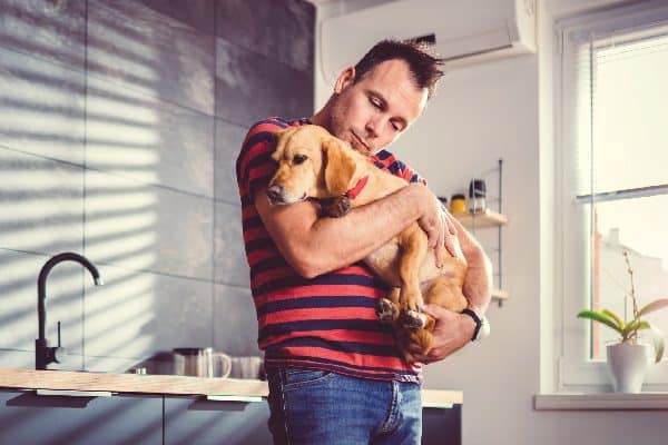 A man holding a dog in an apartment kitchen.