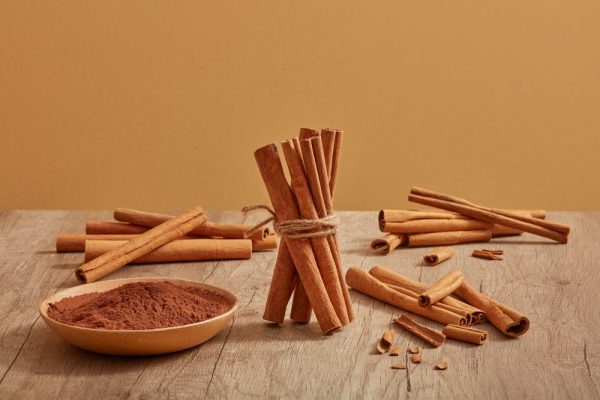 cinnamon sticks are decorated on a wooden table with cinnamon powder placed on a dish