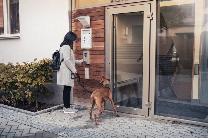 Woman entering password to open door while standing with dog at entrance of apartment