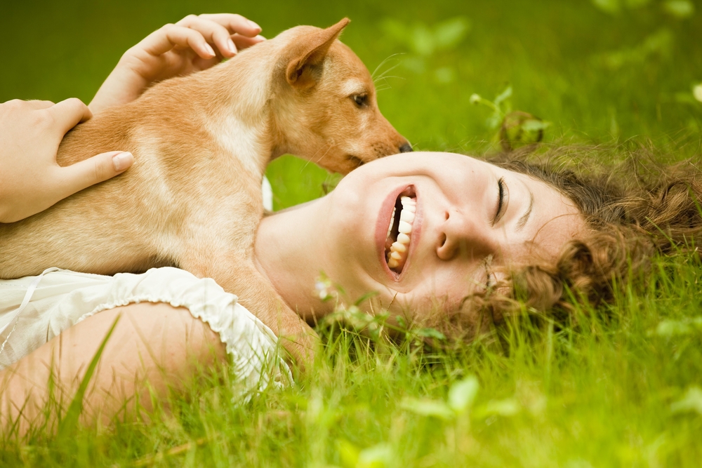 Happy woman lying on the grass with her dog in the park