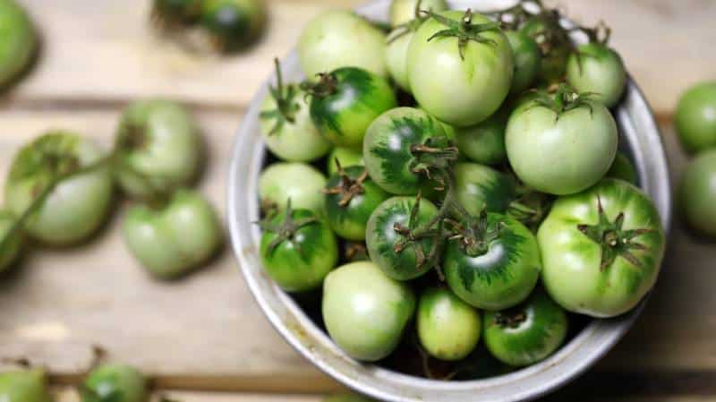 Green tomatoes in a bowl on a wooden surface