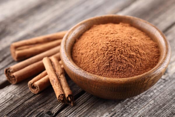 a bowl of cinnamon powder and sticks on wooden background