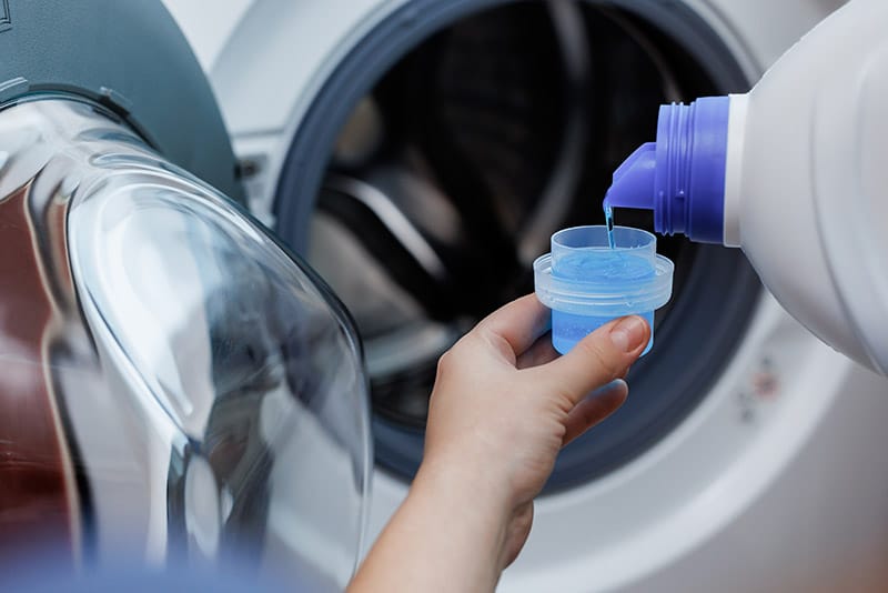 person pouring liquid detergent to the cap for laundry