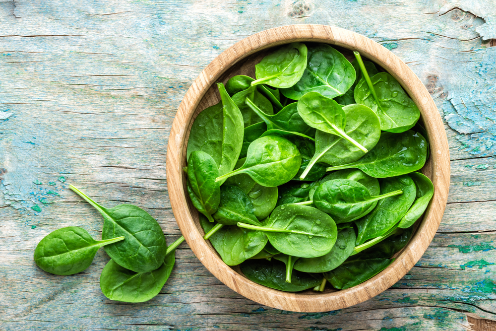 Fresh baby spinach leaves in a bowl on a wooden background