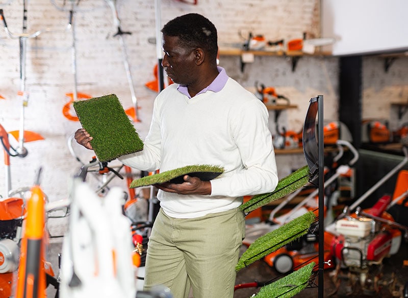 Friendly man deciding on artificial turf from assortment in garden equipment shop