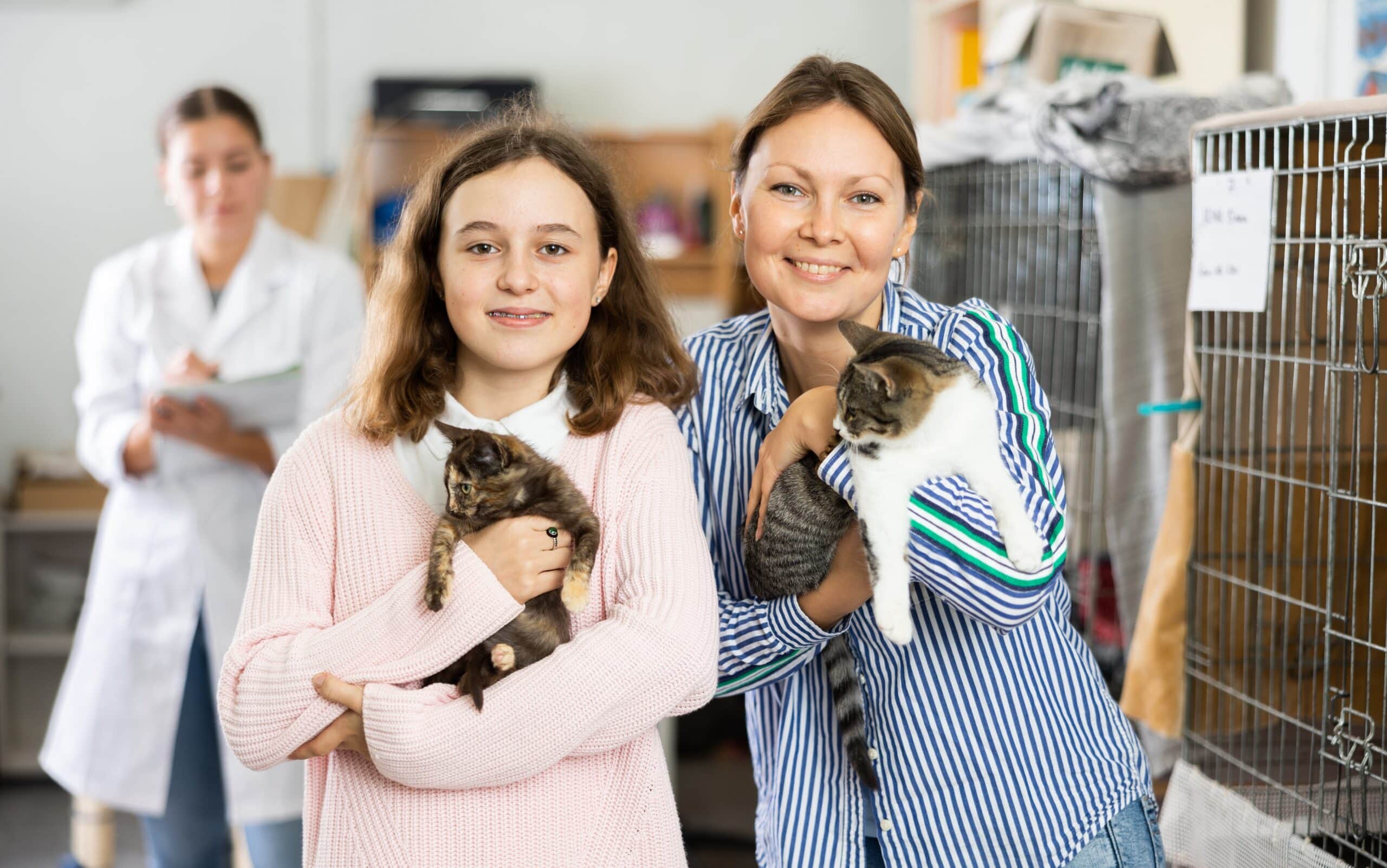 Girl and woman owners holding-cats-in shelter to adopt