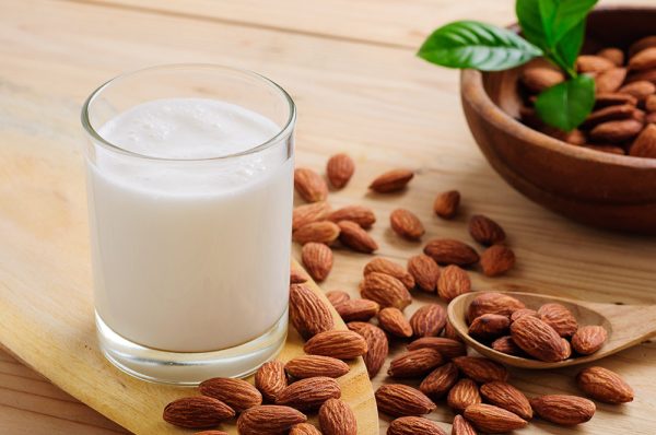 a glass of Almond milk surrounded with almonds