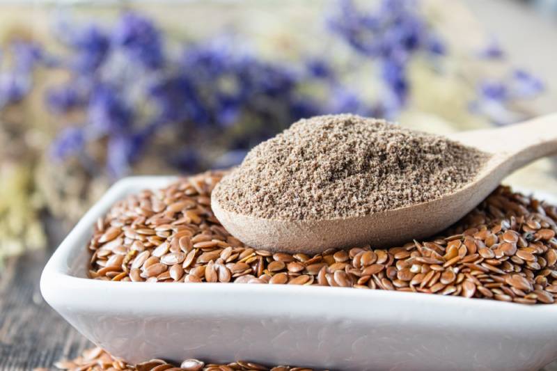 crushed flax seed in a wooden spoon on a pile of flaxseed