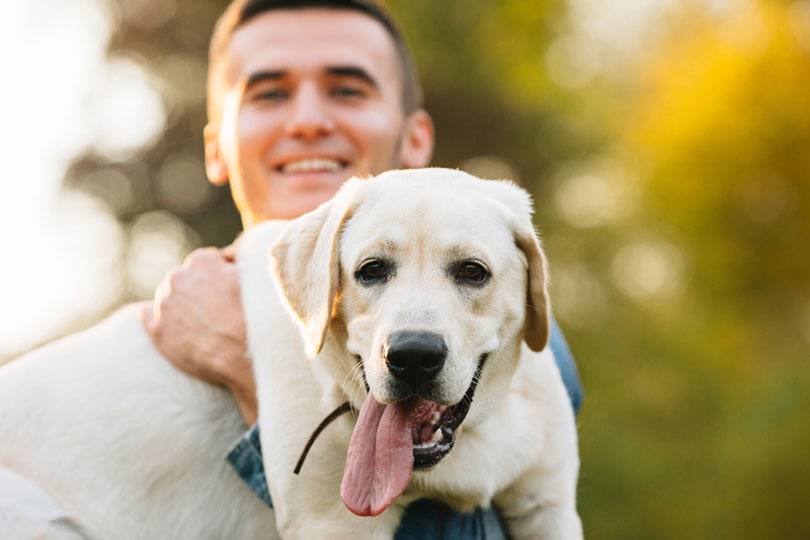 man-holding-his-labrador-dog-and-smiling-at-sunset