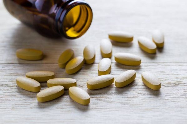 pills of vitamin C spilled out open container on wood background