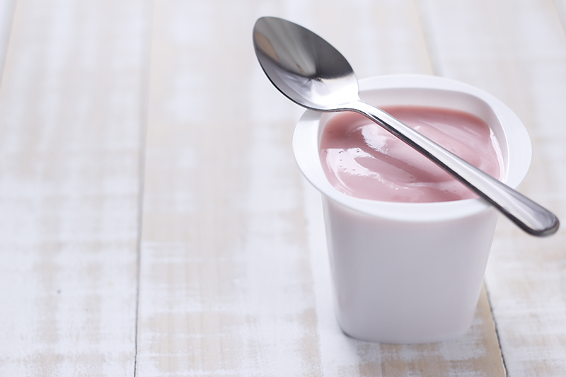 strawberry yogurt in white plastic cup with spoon on wooden white background