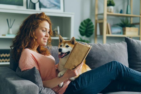 A Woman Reading a Book on a Sofa with a Dog