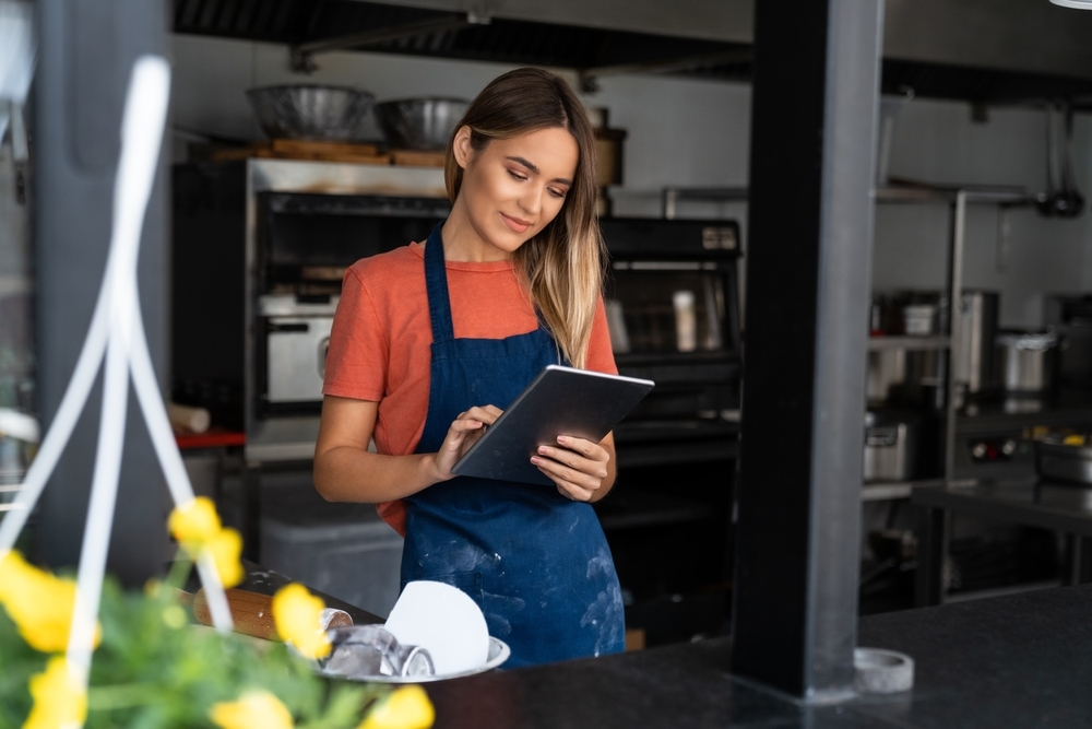 Beautiful young concentrated woman using digital tablet managing a bakery