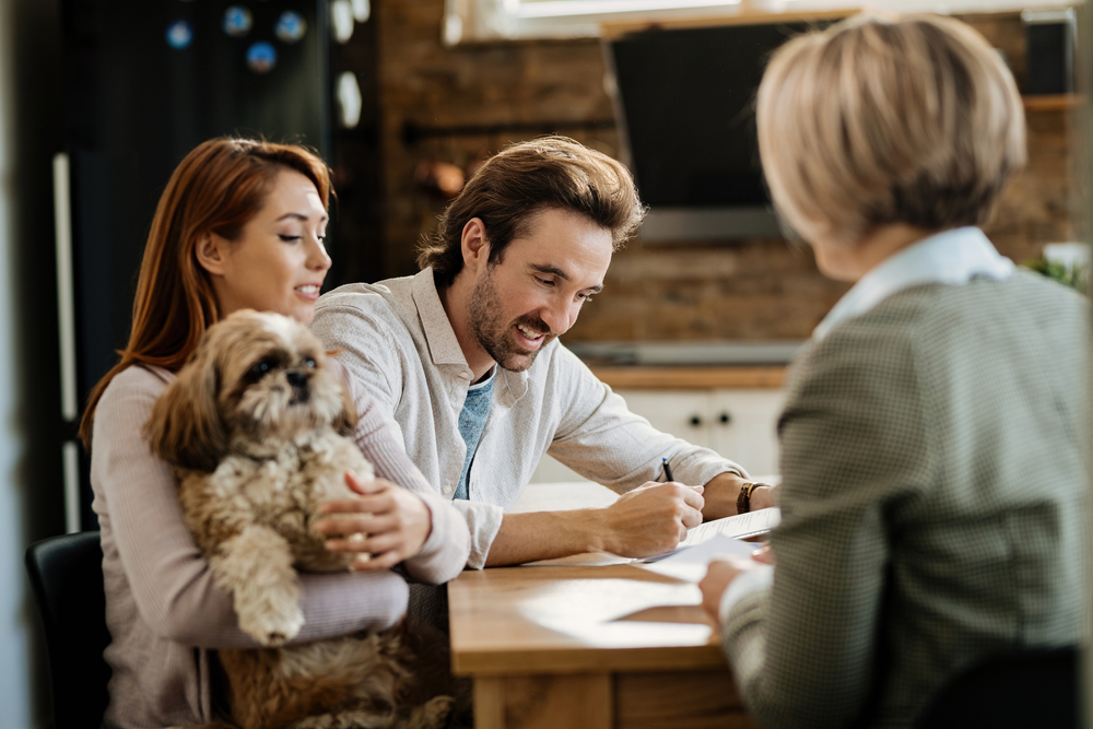 Happy man signing a contract while being with his wife on a meeting with financial advisor