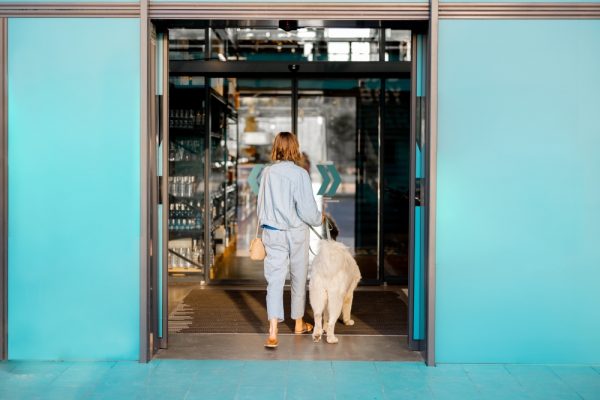Woman with white dog entering supermarket with beautiful turquoise sliding doors