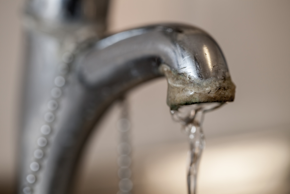 Selective focus on the hard water deposit of a running kitchen or bathroom faucet