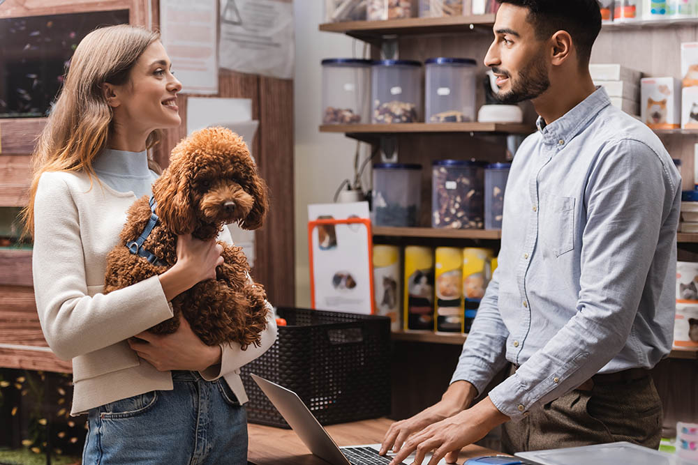 smiling woman holding a puppy and talking to a man in a pet shop