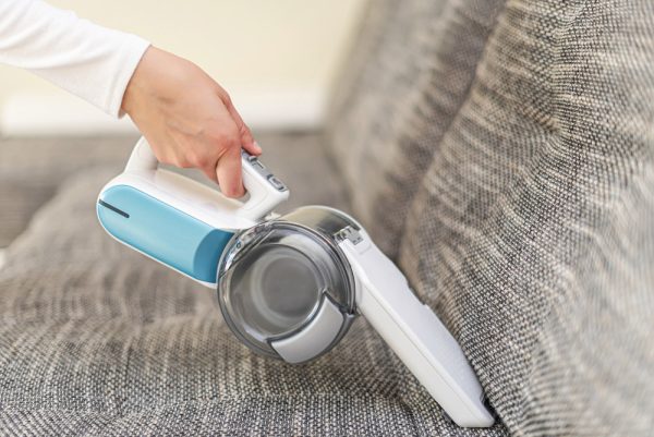 woman cleaning the sofa with handheld vacuum cleaner