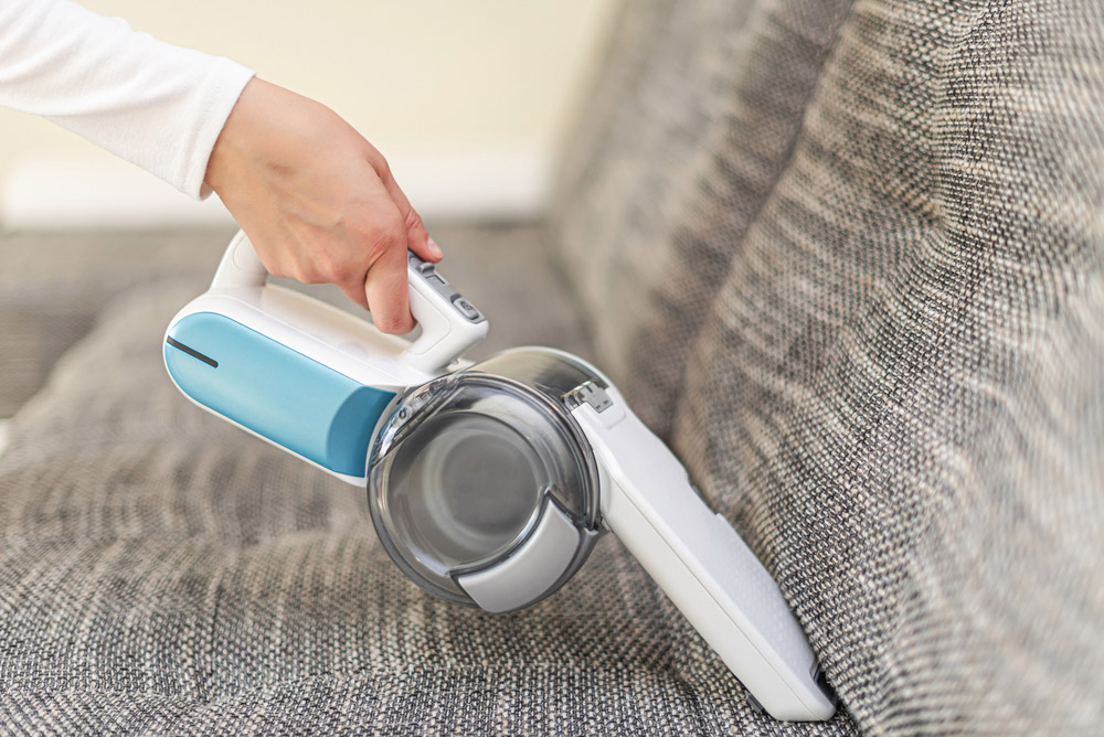 woman cleaning the sofa with handheld vacuum cleaner