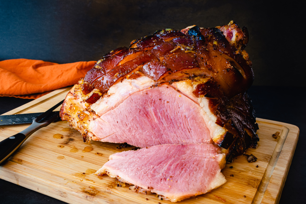 Sliced bone in glazed ham on a wooden cutting board