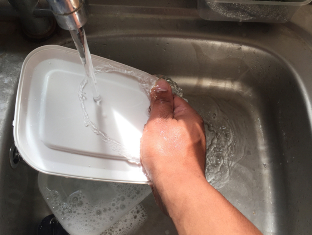 man hand washing his lunch box plastic container