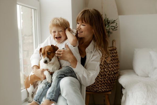 mother and toddler cuddling with a dog near the window