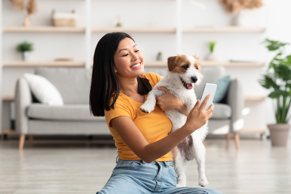 woman sitting on floor taking selfie with her playful cute dog jack russel terrier puppy