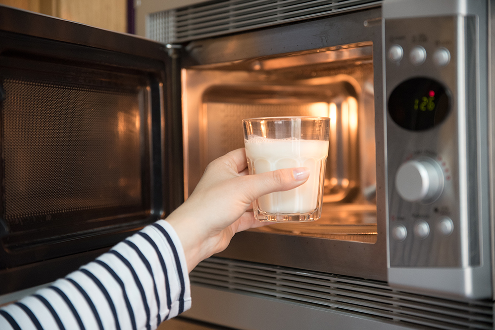 woman warming a glass of milk in the microwave