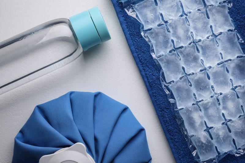 Bottle of water, ice pack, cold compress and towel on white background, flat lay