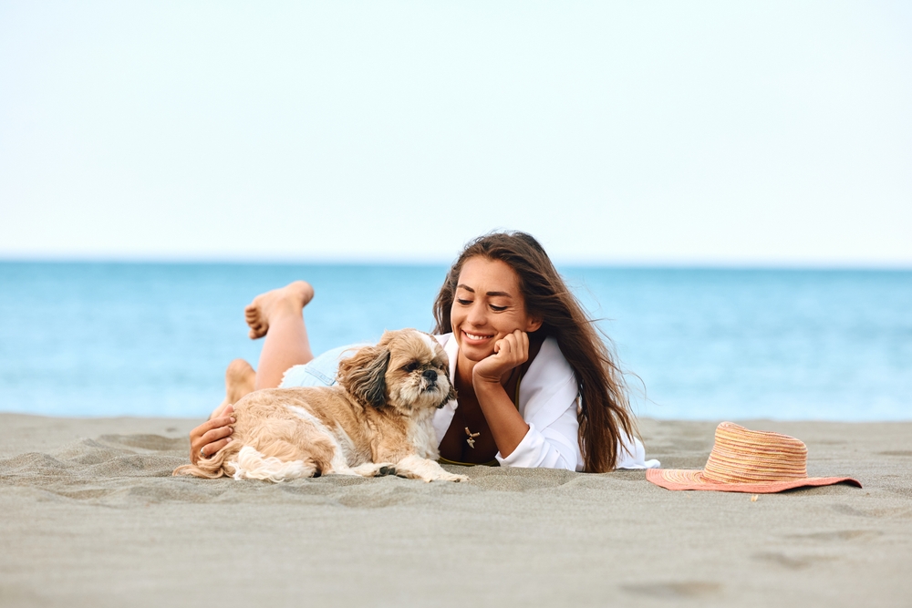 woman with a dog relaxing on sand during summer vacation
